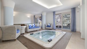 Et moderne poolområde indendørs med jacuzzi, fletmøbler og store vinduer.