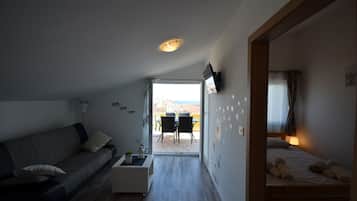 Ein modernes, kompaktes Wohnzimmer mit Sofa, einem kleinen Tisch, einem Bett und einem Essbereich mit Stühlen.