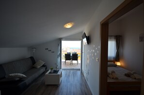 Un espacio habitable moderno y compacto con sofá, una mesita, cama y una zona de comedor con sillas.