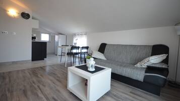 Ein modernes Wohnzimmer mit grauem Sofa, weißem Couchtisch und einem Essbereich mit Tisch und Stühlen.