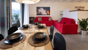 Ein Essbereich mit einem Holztisch, gedeckt für vier Personen, umgeben von roten Sofas und einem großen Fenster mit Blick ins Freie.