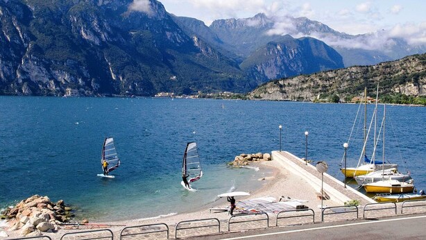 Eine Küstenlandschaft mit Windsurfaktivitäten, einer felsigen Küstenlinie und Bergen im Hintergrund.