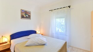 Une chambre à coucher avec un lit, une table de chevet, une lampe, une fenêtre avec des rideaux et un tableau au mur.
