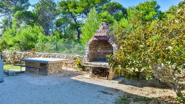 Un espace barbecue extérieur avec un grill en pierre, un banc et une table.
