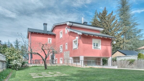 Un edificio de dos pisos con fachada roja, pared de piedra y un pequeño jardín con un árbol y piedras para pisar.