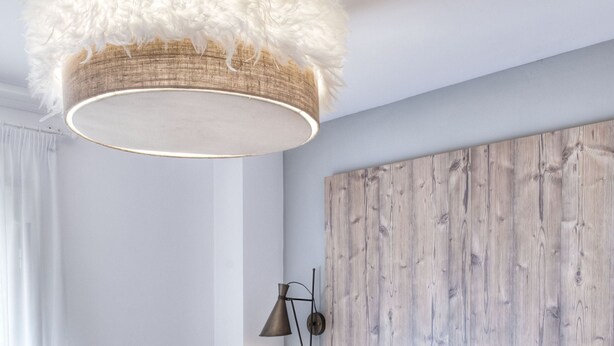 Een moderne slaapkamer met twee bedden, een houten hoofdbord, een lamp met veren en een nachtkastje met lamp.