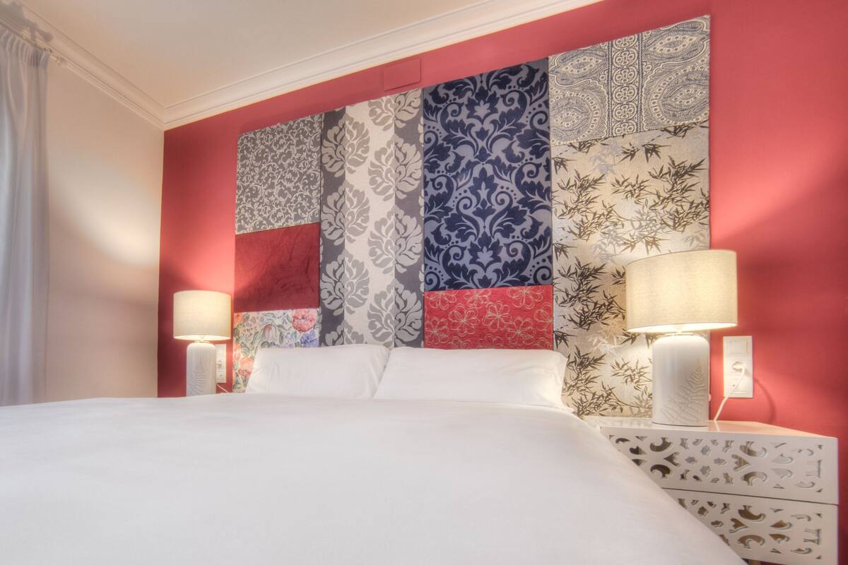 A hotel room with a large bed, two bedside lamps, and a wall with a patchwork of different patterns.