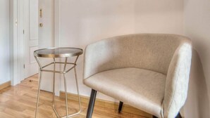 Een kamer met een ronde spiegel, een rond metalen tafeltje en een beige fauteuil.