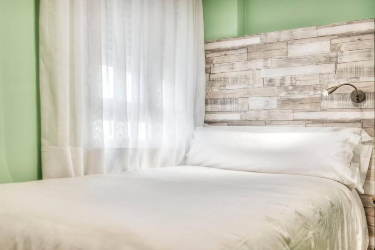 A bedroom with a wooden headboard, white bedding, and a window with sheer curtains.