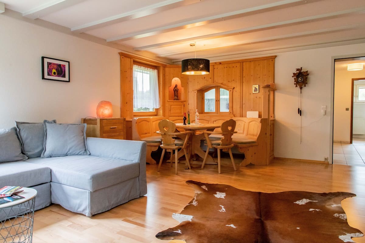A cozy room with a sofa, wooden dining table, chairs, a cowhide rug, and a wooden ceiling.