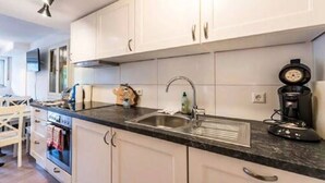 Une cuisine moderne avec des meubles blancs, un évier en acier inoxydable et une machine à café.