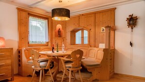 Une pièce chaleureuse aux murs en bois, avec une table ronde, quatre chaises, un banc et un buffet en bois.