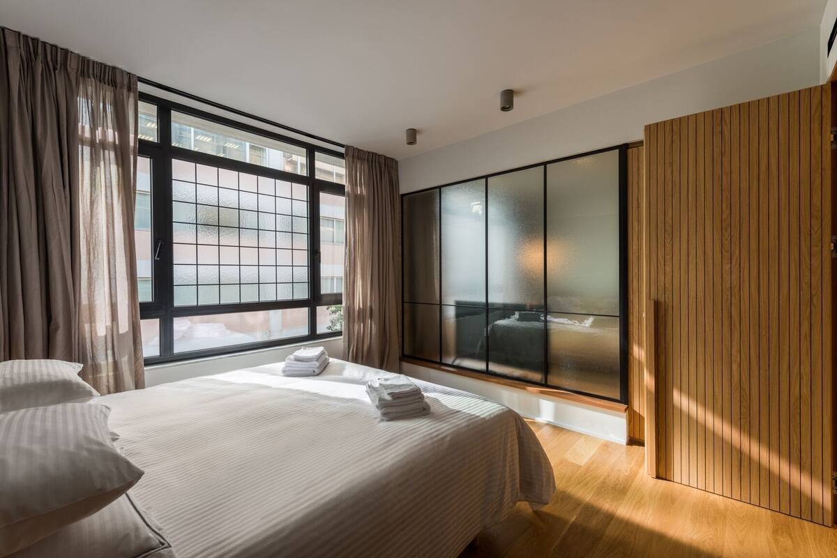 A modern hotel room with a large bed, a sliding glass door, and a wooden wardrobe.