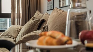 Ett vardagsrum med en soffa, ett bord med en tallrik full av croissanter, en kaffekanna och konst på väggen.