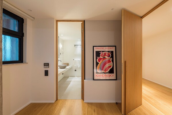 Un pasillo con piso de madera, una puerta que da al baño y un cartel enmarcado en la pared.