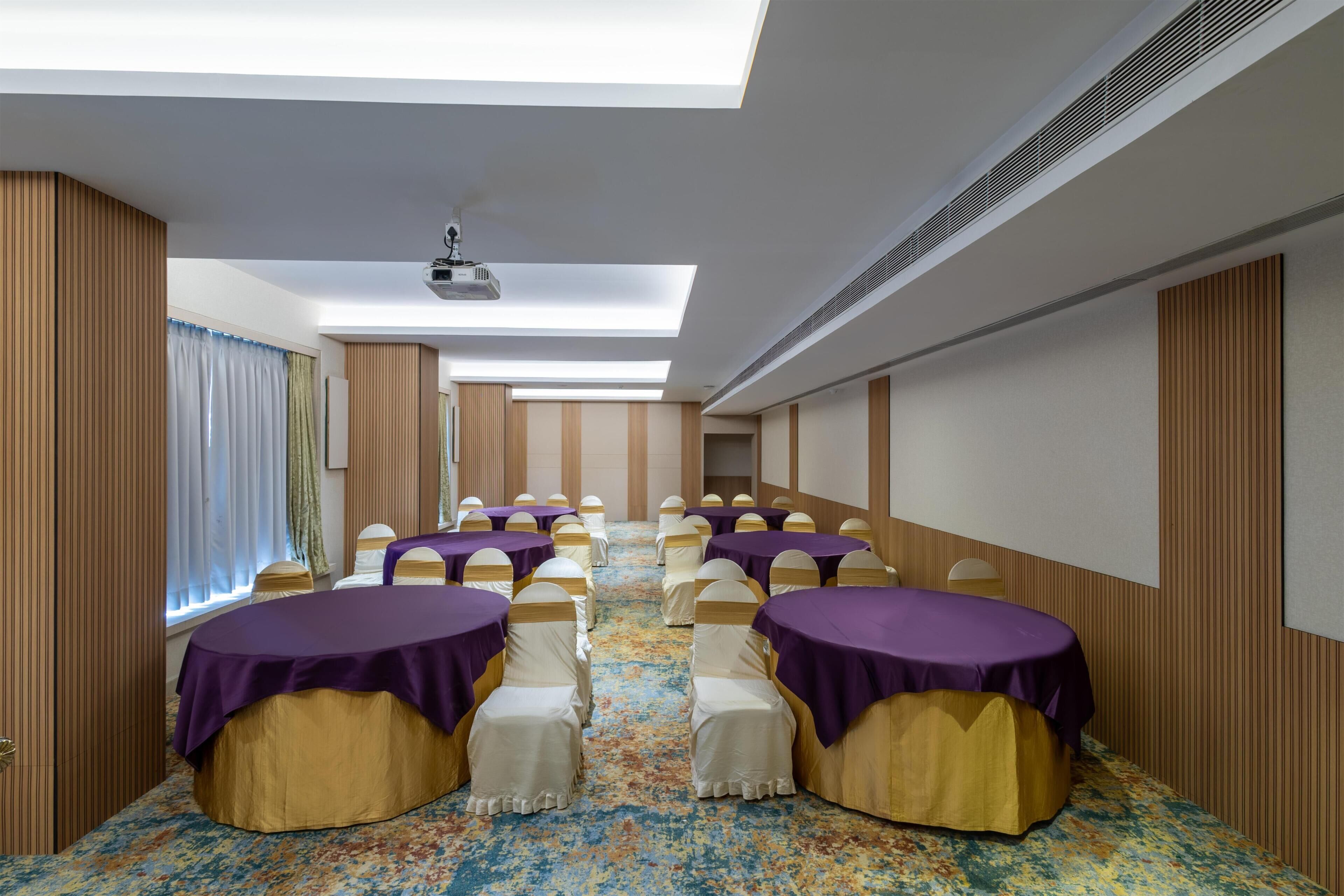 A conference room with rows of tables, chairs, and a projector on the ceiling.
