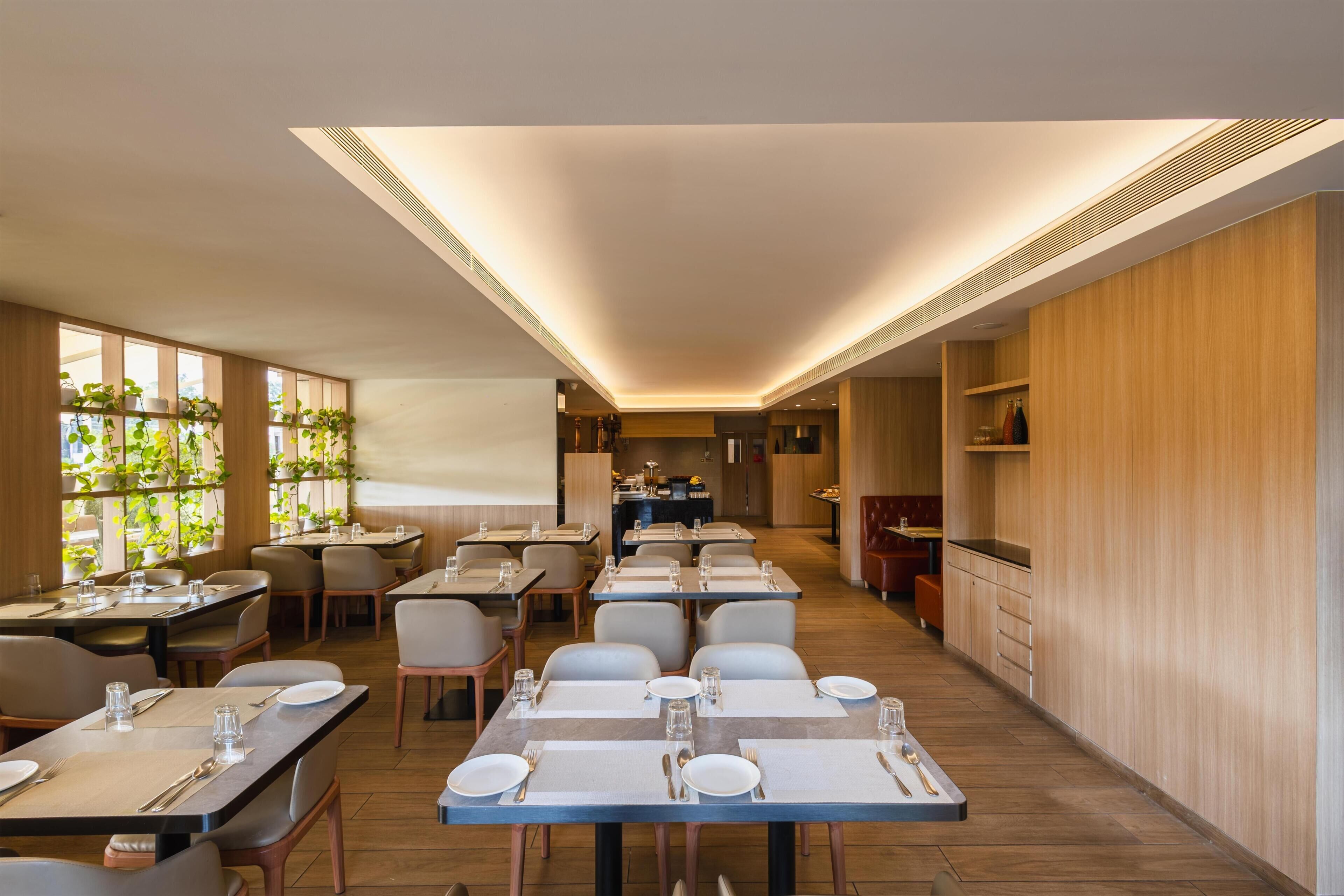 A modern restaurant with wooden flooring, tables set with plates and cutlery, and a kitchen in the background.