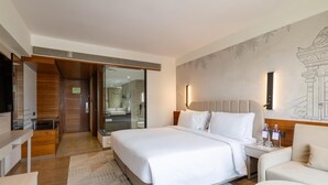 Una habitación de hotel moderna con una cama grande, una zona de estar, un baño con ducha de vidrio y un mural en la pared.
