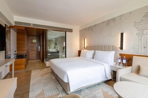 Una habitación de hotel moderna con una cama grande, una zona de estar, un baño con ducha de vidrio y un mural en la pared.