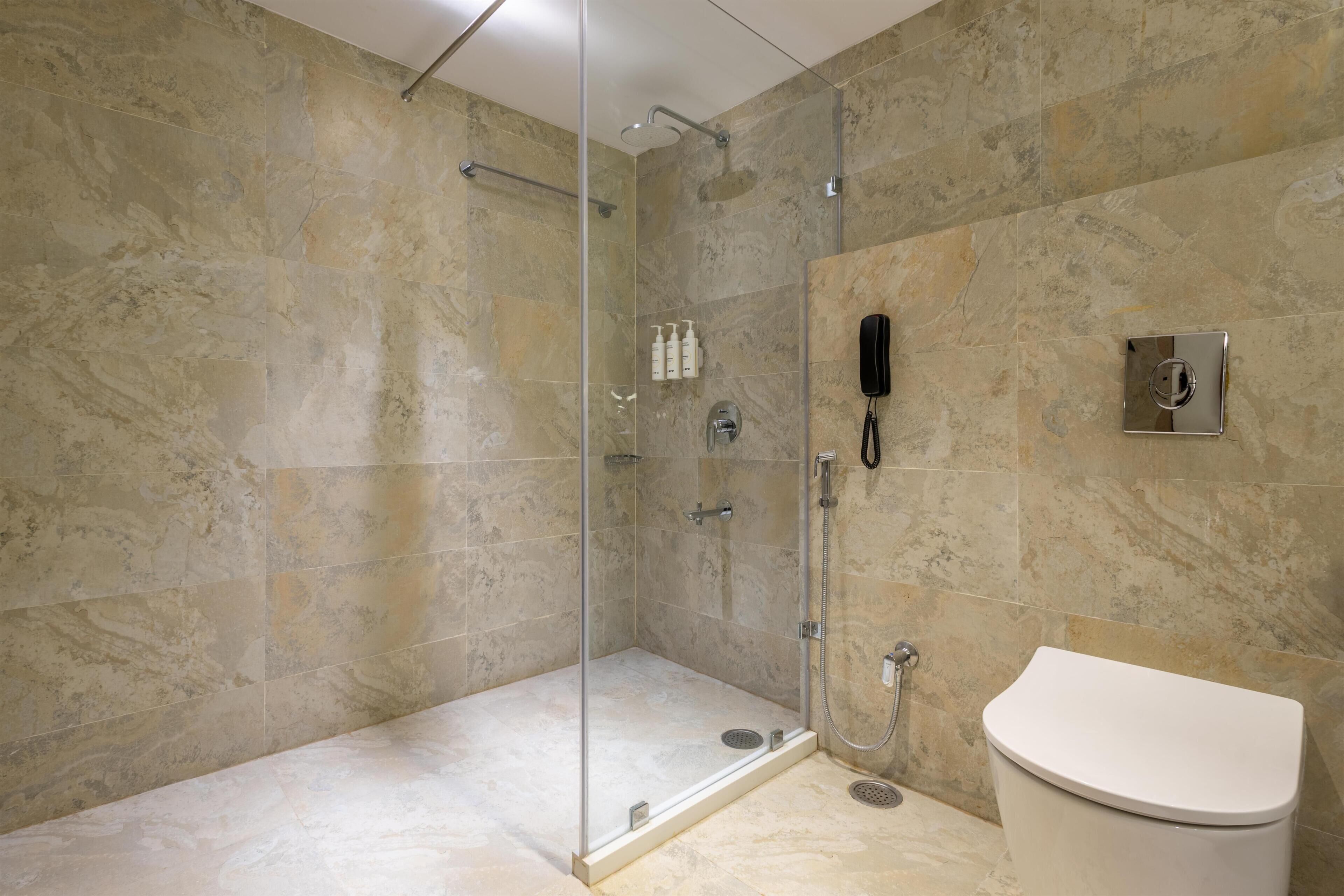 A bathroom with a glass-enclosed shower, a toilet, and a wall-mounted phone.