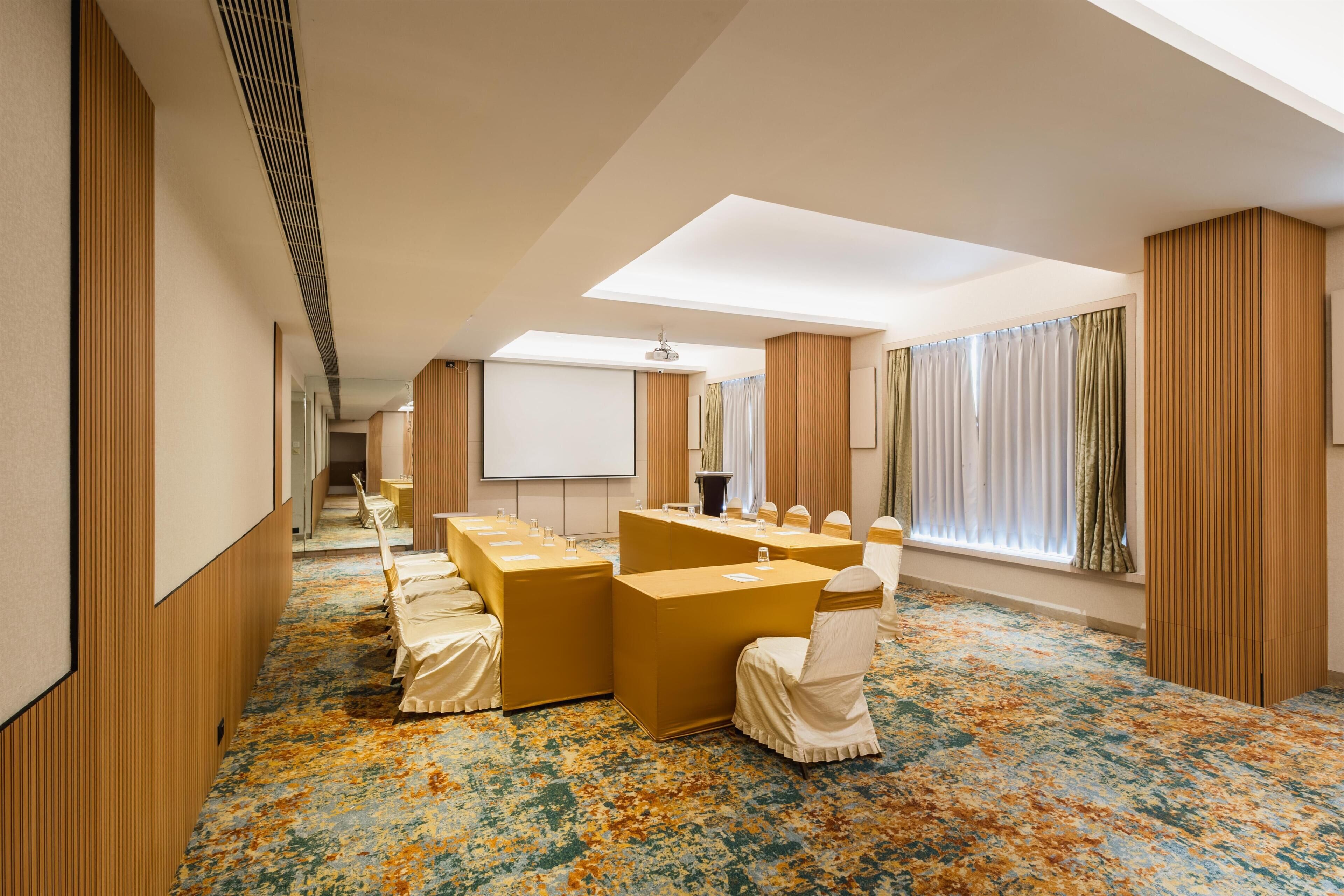 Een vergaderzaal met een lange tafel, stoelen, een projectiescherm en een groot raam met gordijnen.