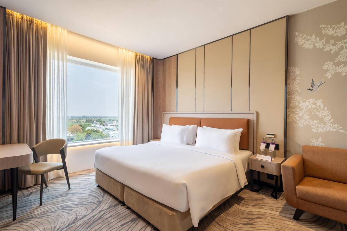 Quarto de hotel com uma cama grande, uma escrivaninha, uma cadeira, um criado-mudo e vista para a cidade.