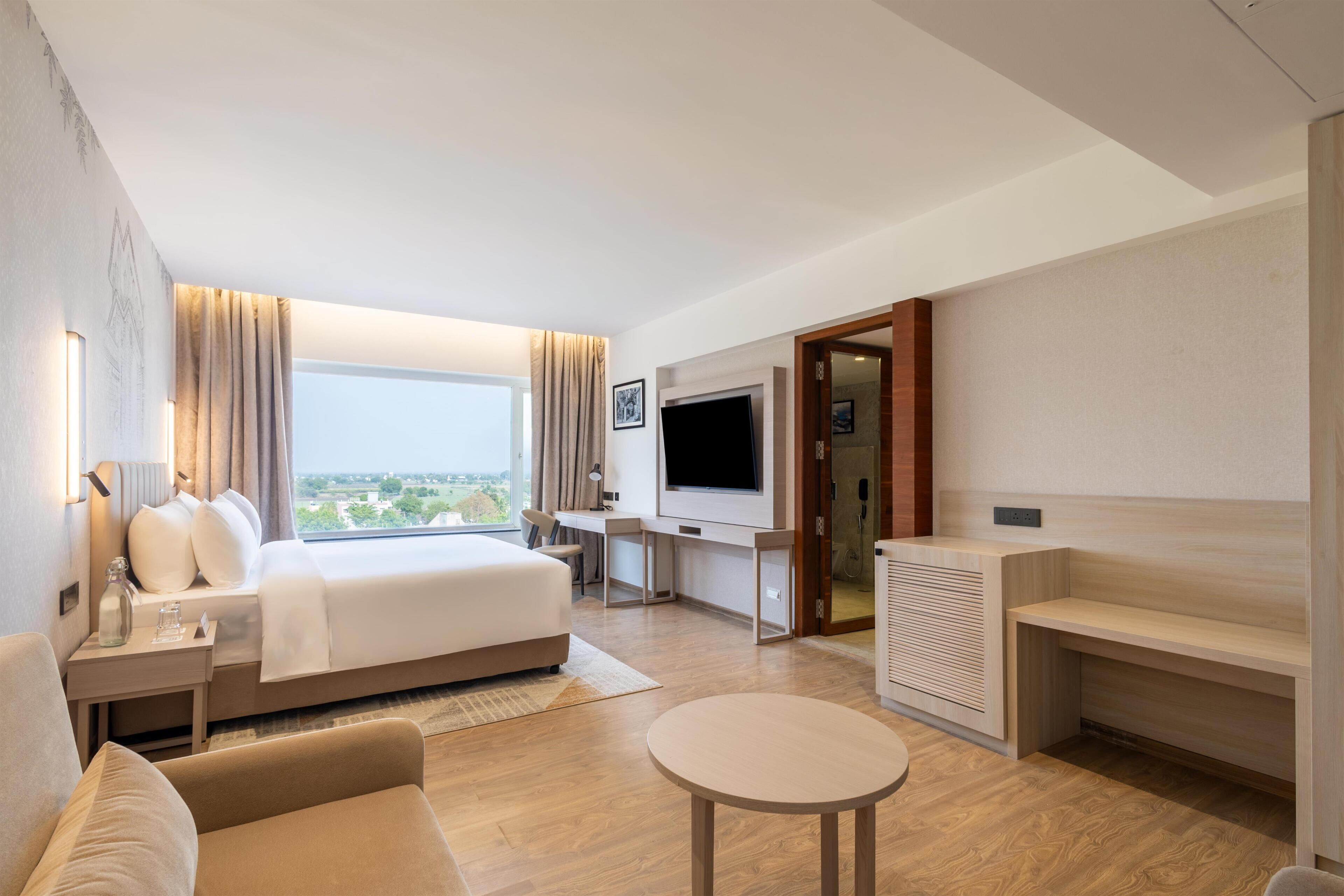 Ein Hotelzimmer mit Bett, Schreibtisch, Fernseher, einer Couch und einem kleinen Tisch.