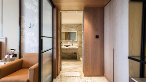 Una habitación de hotel moderna con piso de madera, baño de mármol y una zona de estar con sofá.