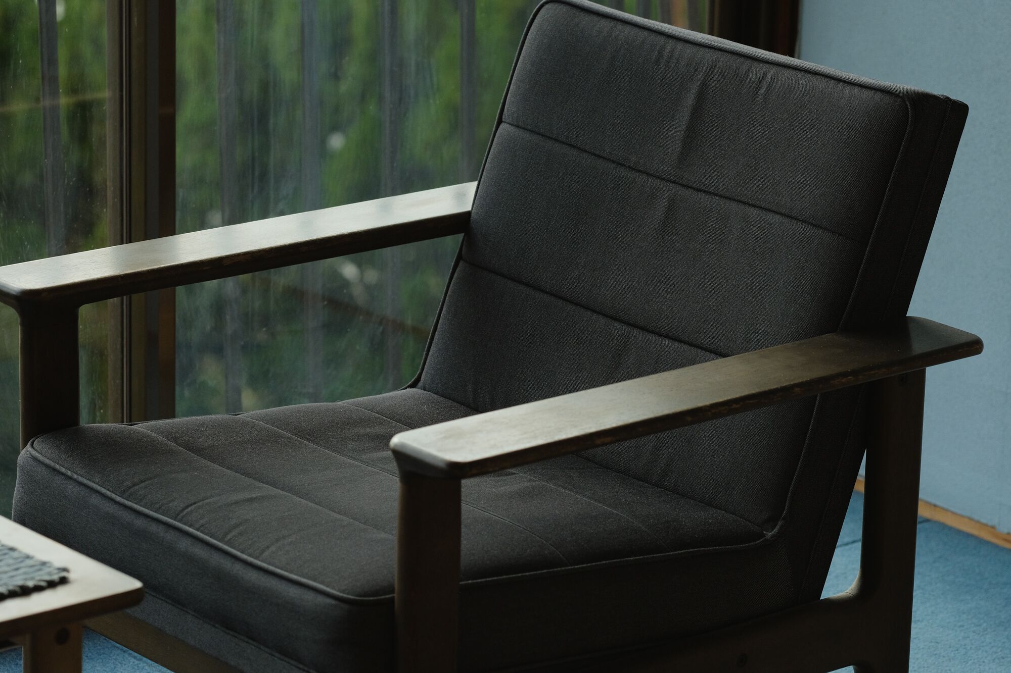 A chair with a high backrest and armrests, positioned near a window with a view of greenery.
