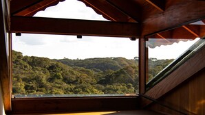 A room with a large window offering a view of a forested hillside. - Hotel Vinícola Davo (Ribeirão Branco)