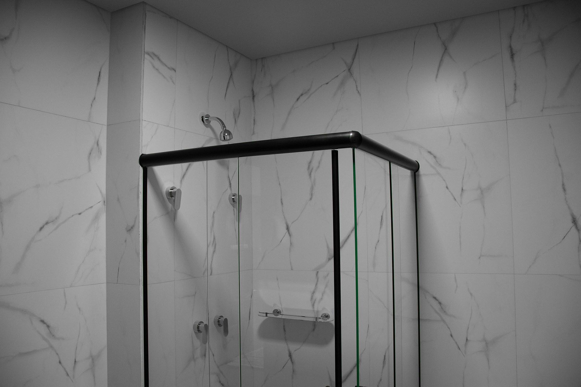 Ducha con cerramiento de vidrio, marco negro y un perchero verde.
