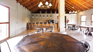 A spacious dining area with a large wooden table and multiple chairs, a brick column, and a kitchen in the background. - Hotel Vinícola Davo (Ribeirão Branco)