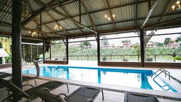 An indoor swimming pool with clear glass walls, lounge chairs, and a view of the surrounding landscape.