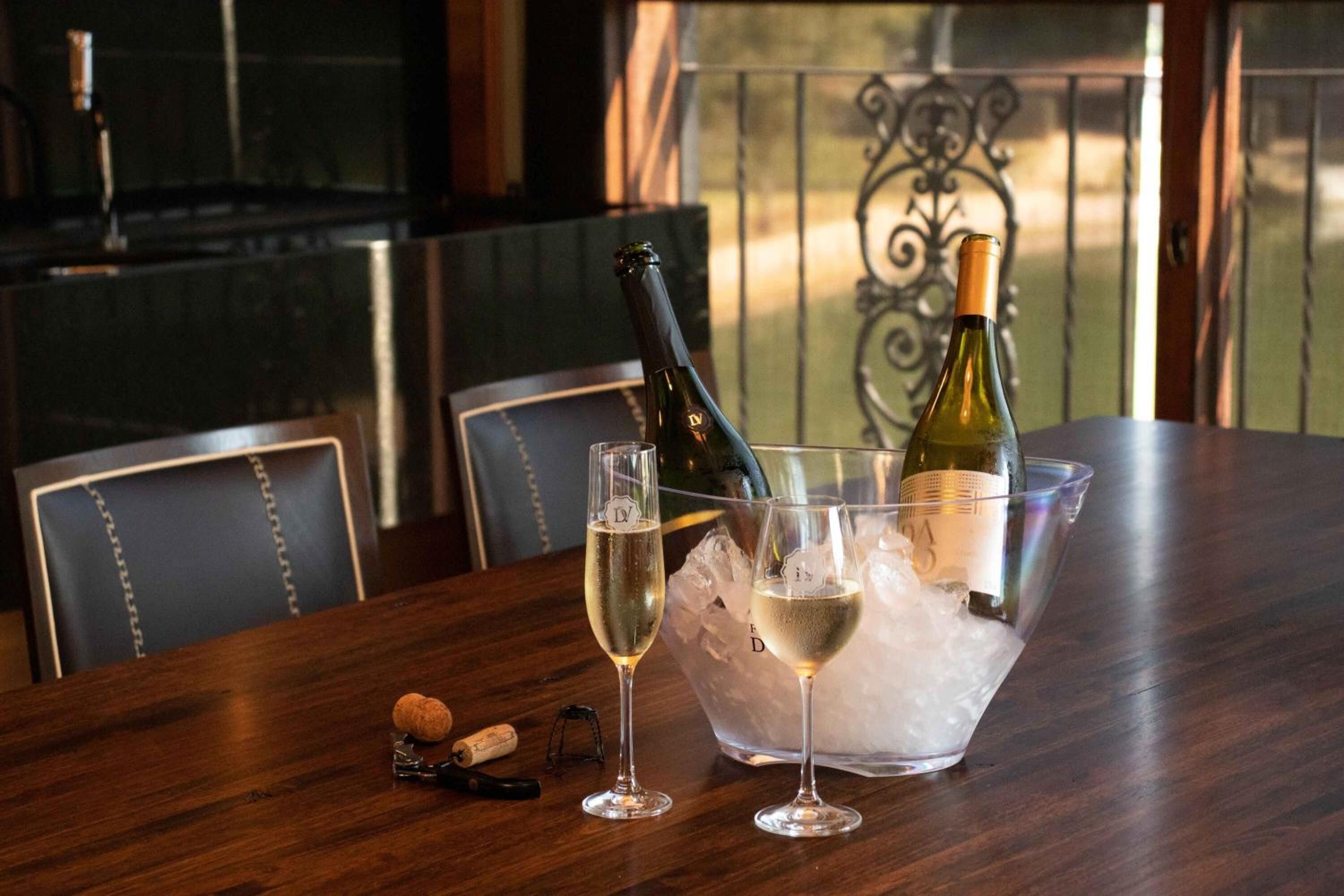 Un tavolo con due bicchieri di vino bianco, una bottiglia di vino, un cavatappi e una bottiglia di vino immersa in un secchio pieno di ghiaccio.