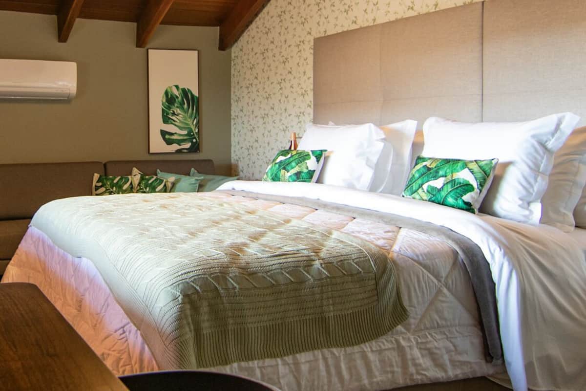 Une chambre à coucher comprenant un lit, une table de chevet, une chaise, un appareil de climatisation et une œuvre d’art accrochée au mur.