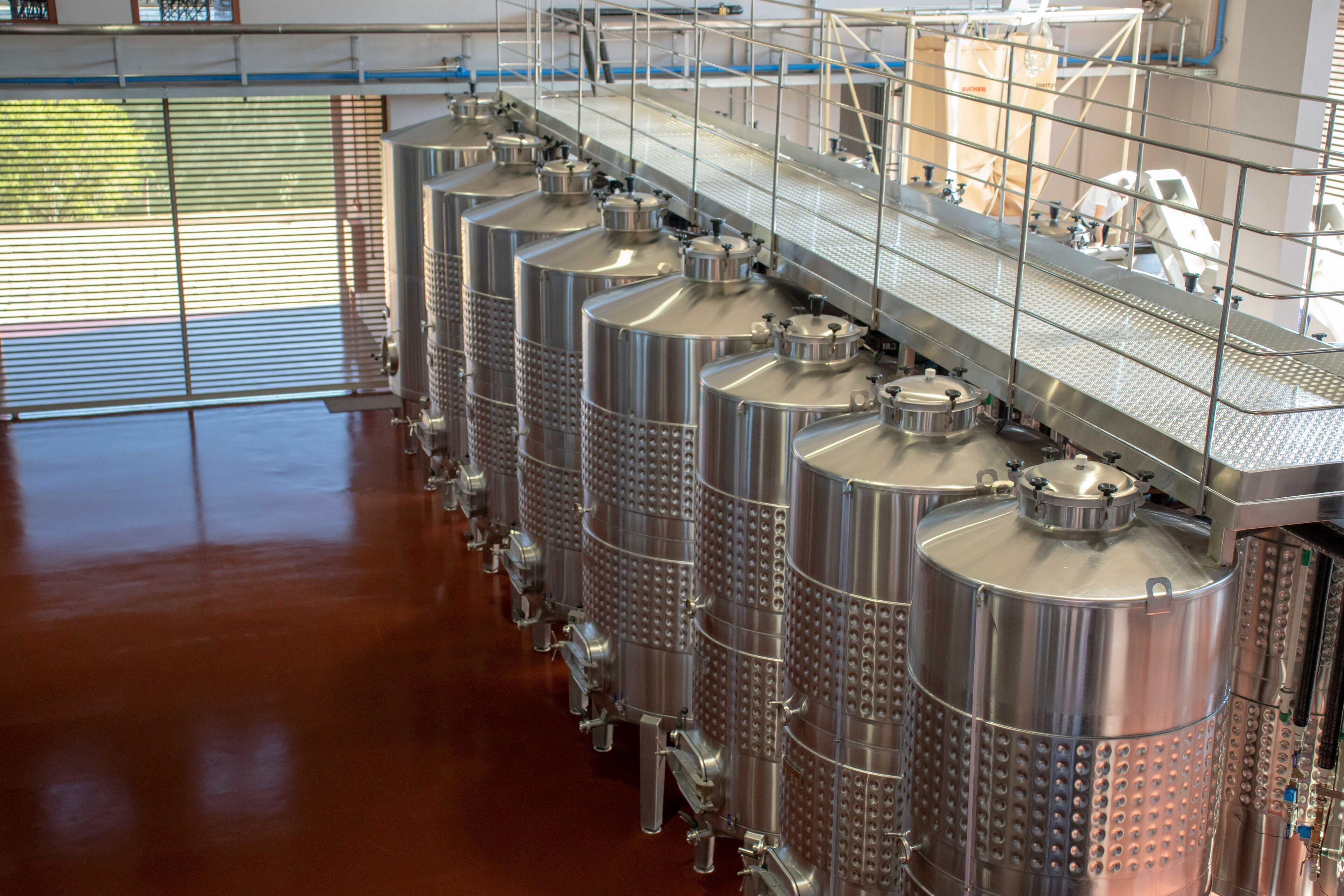Edelstahltanks für die Gärung in einer sauberen, industriellen Umgebung mit poliertem Boden und einem Metallgang darüber.