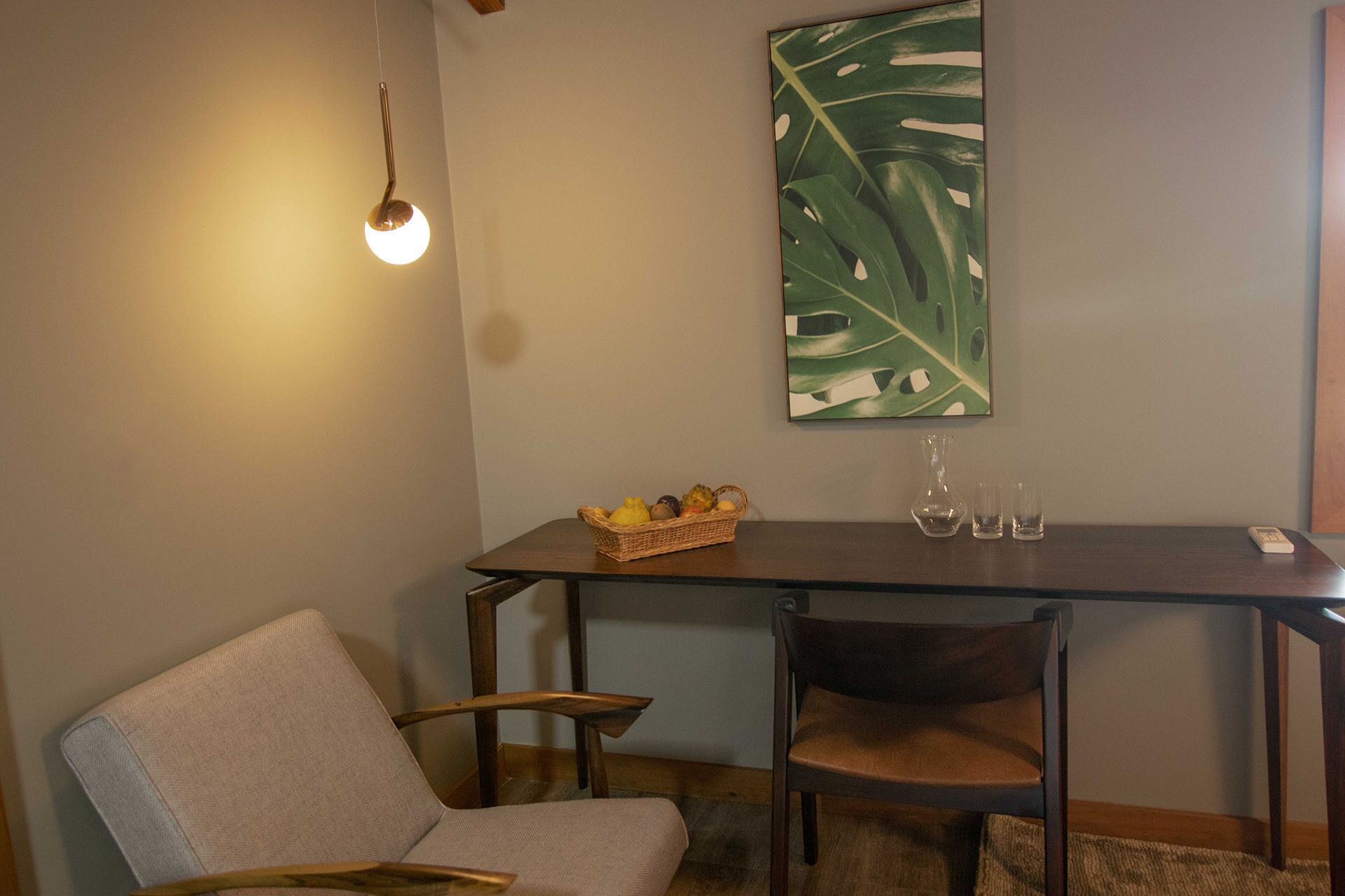 A dining area with a table, chairs, a fruit basket, and a wall-mounted light fixture.
