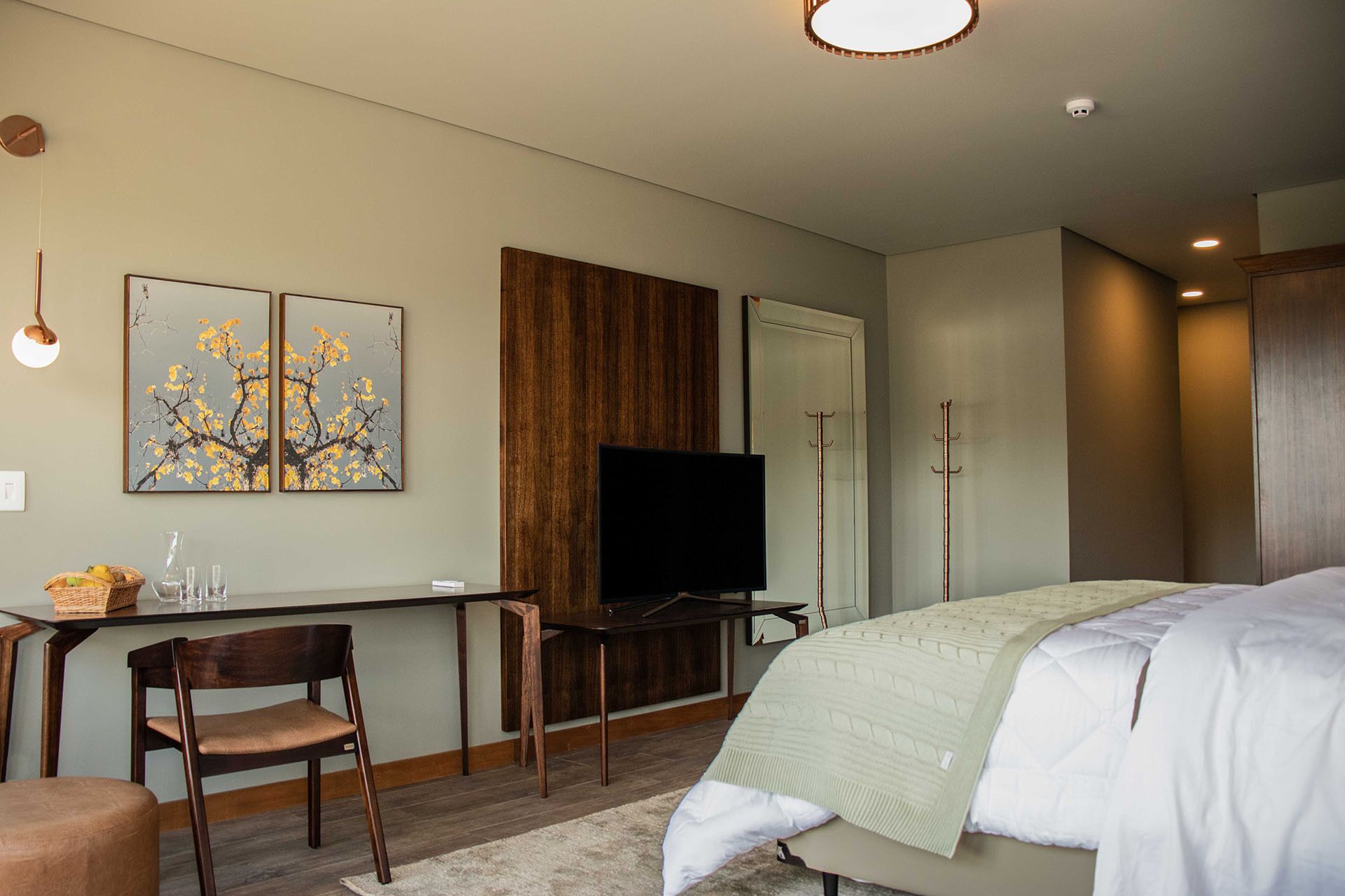 Een slaapkamer met een bed, een bureau, een stoel, een televisie en kunst aan de muur.