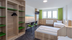 A hotel room with two beds, a desk, chairs, a TV, and a wardrobe. - Sportpark Rabenberg (Breitenbrunn/Erzgeb.)
