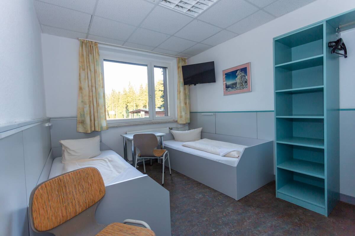 A dormitory room with two single beds, a desk, a chair, a television, and a bookshelf.