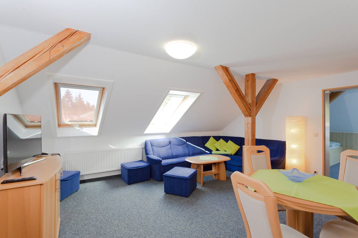 A room with a sloped ceiling, a sofa set, a table, and a TV.