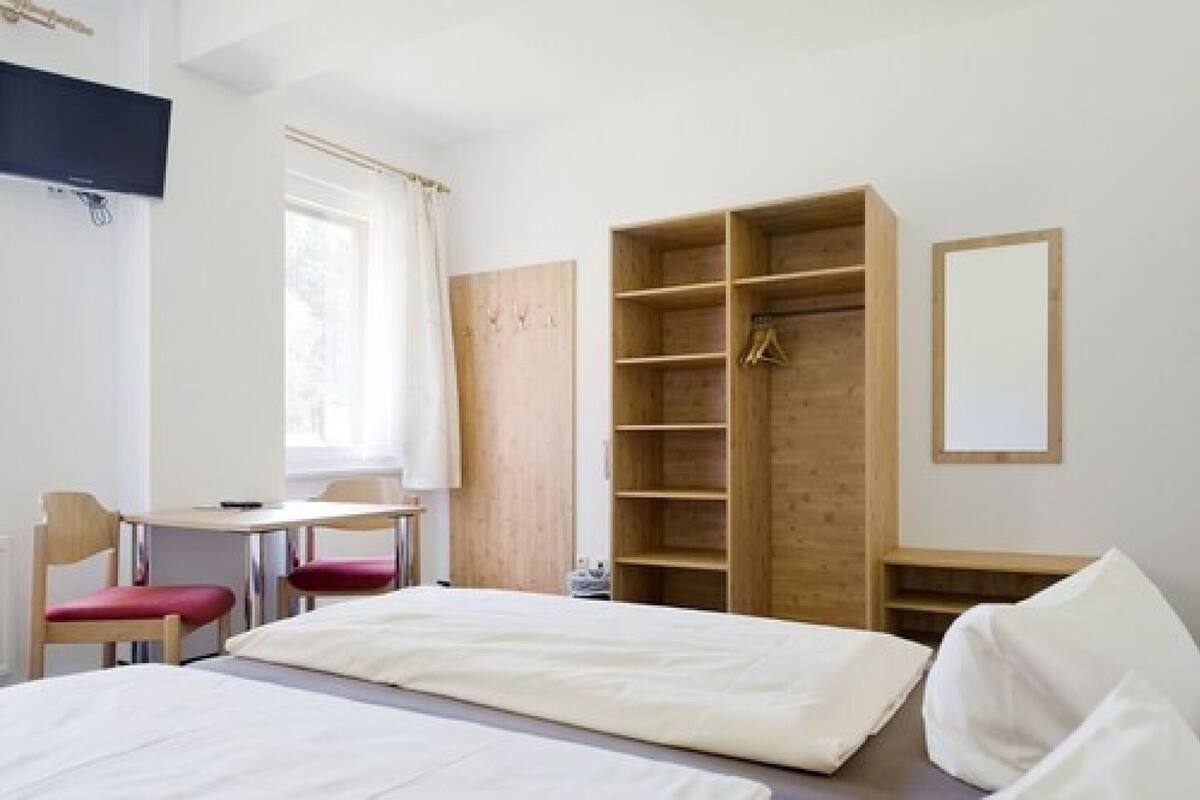 A bedroom with a bed, a desk, chairs, a wardrobe, and a TV.