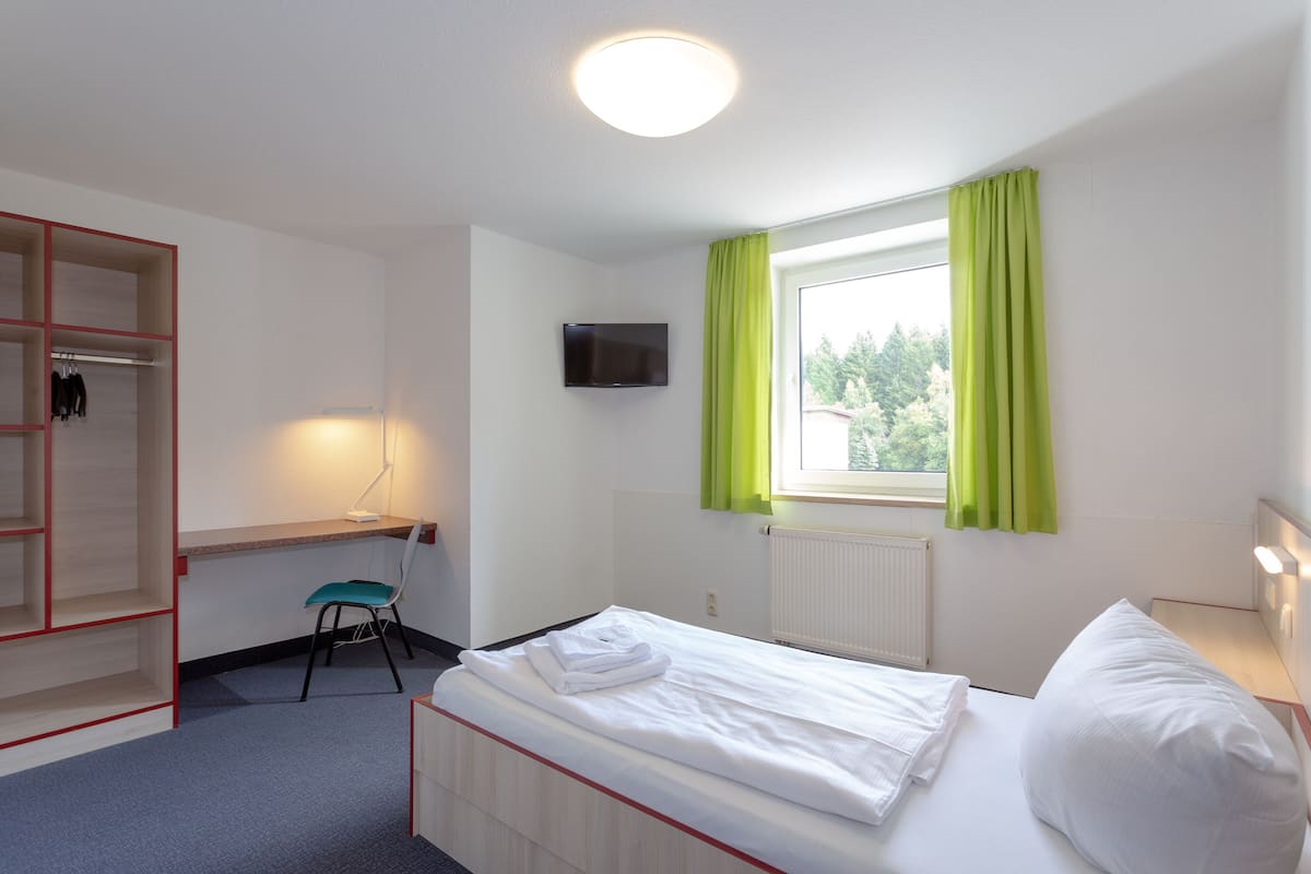 A hotel room with a bed, a desk, a chair, a TV, and a window with curtains.