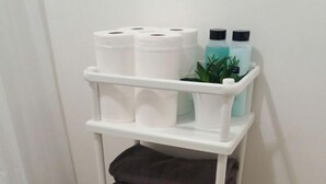 Un armadietto bianco con scaffali che contengono asciugamani, articoli da toilette e una pianta.