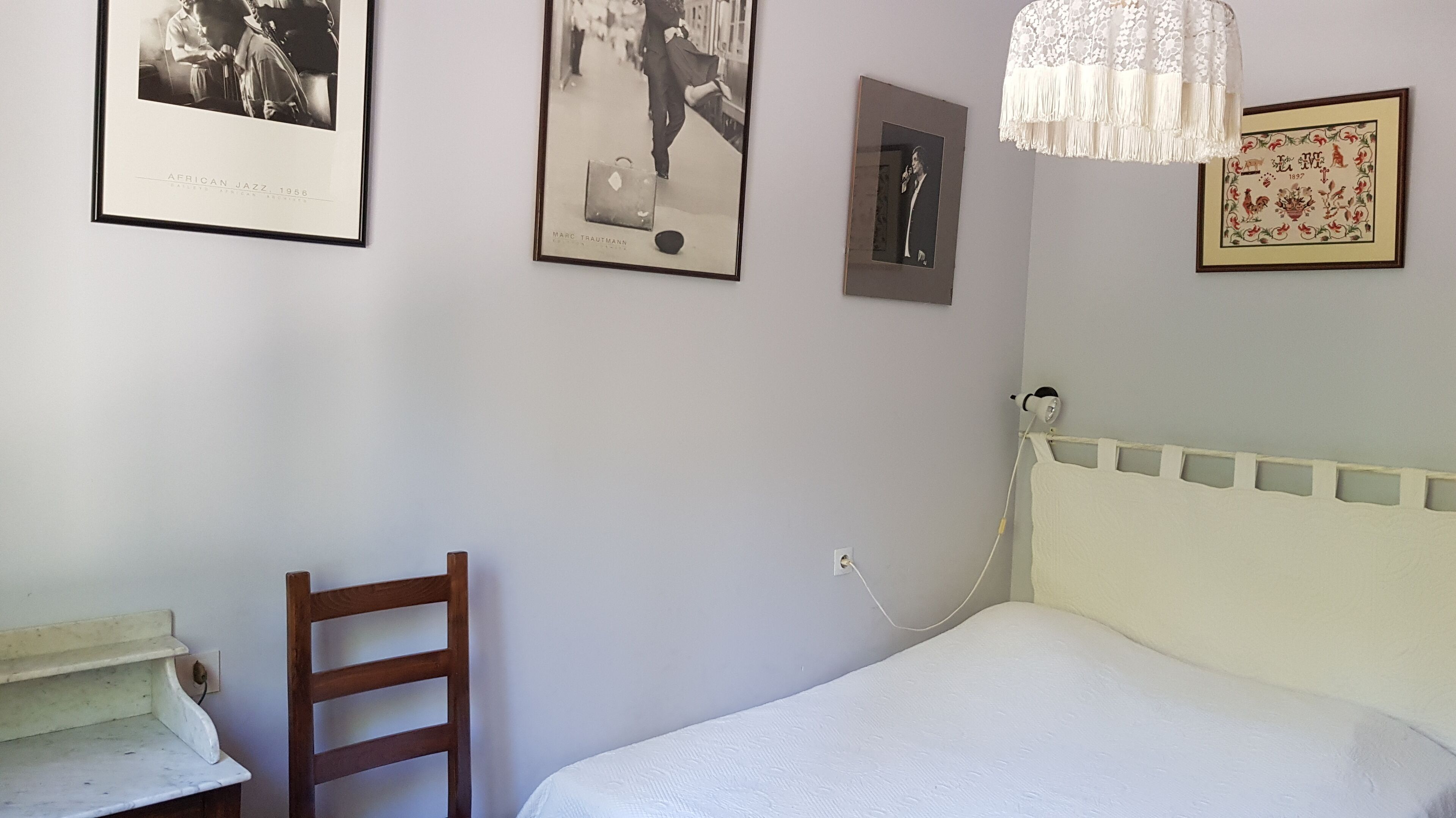 Une chambre à coucher avec un lit, une chaise en bois et trois tableaux encadrés accrochés au mur.