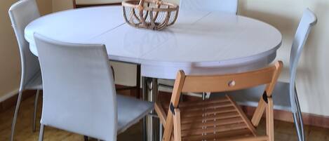 A dining area with a round table, four chairs, a woven basket, and a framed picture on the wall.