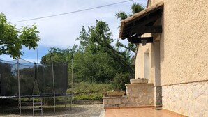 Un espace extérieur aménagé avec un trampoline, un bac à fleurs en pierre contenant des plantes et un bâtiment doté d’une façade en pierre.