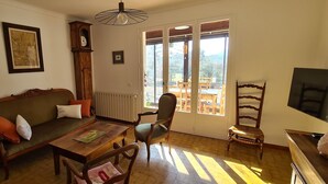 Un salon chaleureux avec un canapé, une table en bois et une chaise. Il y a une horloge au mur et une fenêtre donnant sur l’extérieur.