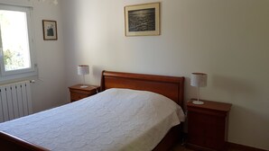 Une chambre avec un lit en bois, deux tables de chevet avec des lampes, un radiateur, une fenêtre et un tableau encadré au mur.