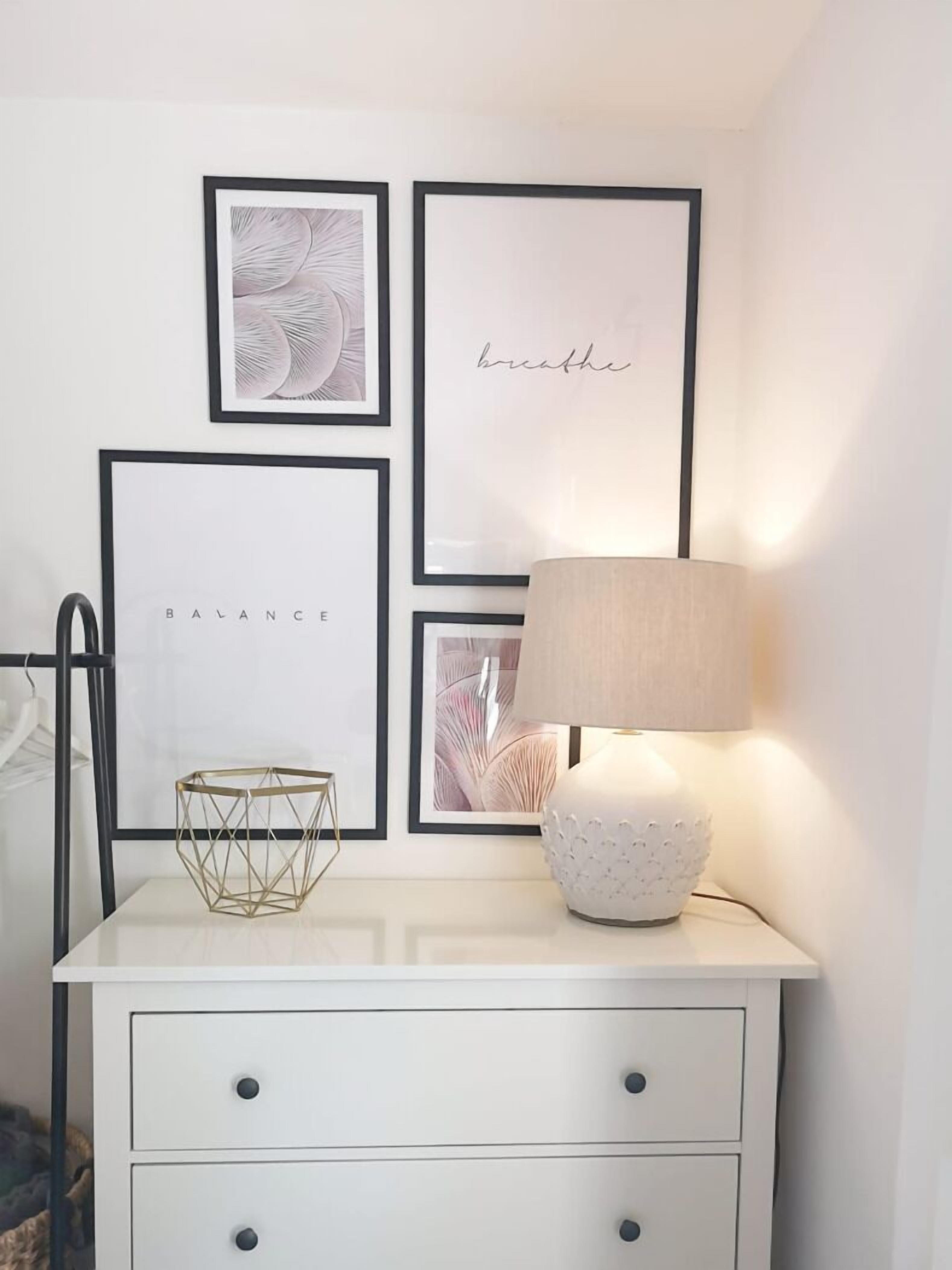 A white bedside table with a lamp, a geometric gold bowl, and framed artwork on the wall.